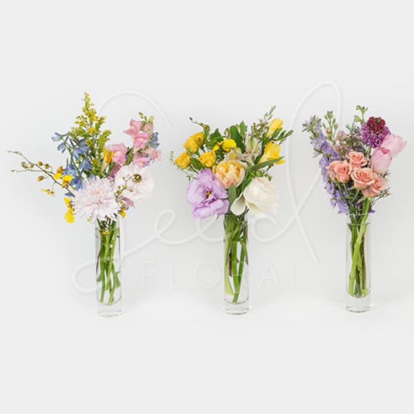 Three tall bud vases with assorted pastel flowers in pink, yellow, lavender, and white.