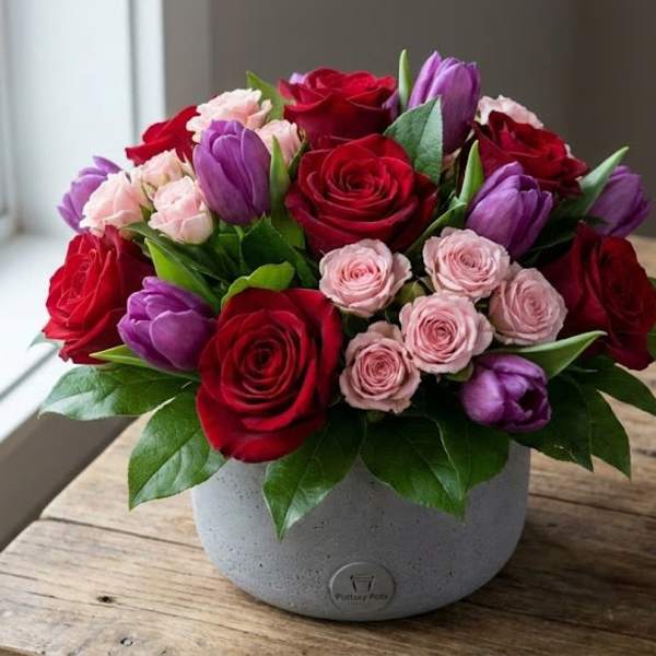 Bouquet of red roses, pink spray roses, and purple tulips in a gray vase