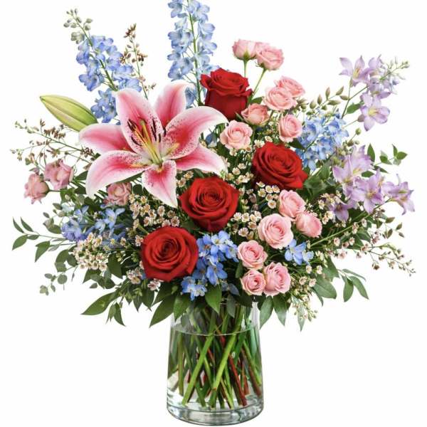 Bouquet of red and pink roses with lilies and blue flowers in a glass vase