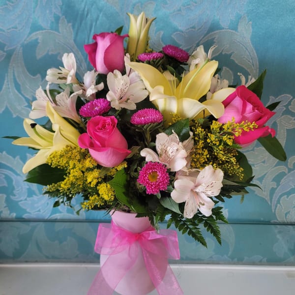 Bouquet of pink roses, lilies, and mixed flowers in a pink vase with ribbon