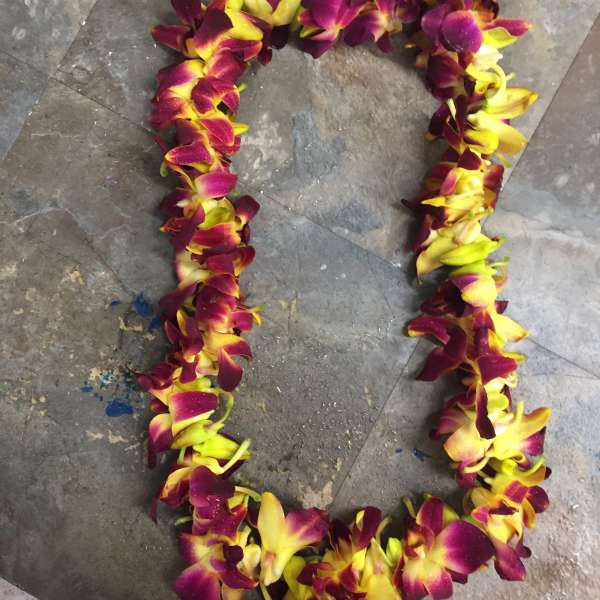 A purple and yellow orchid lei laid in a loop on a stone floor.