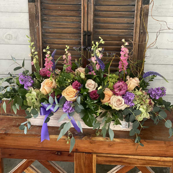 Low floral arrangement with roses, purple blooms, and greenery in a white container