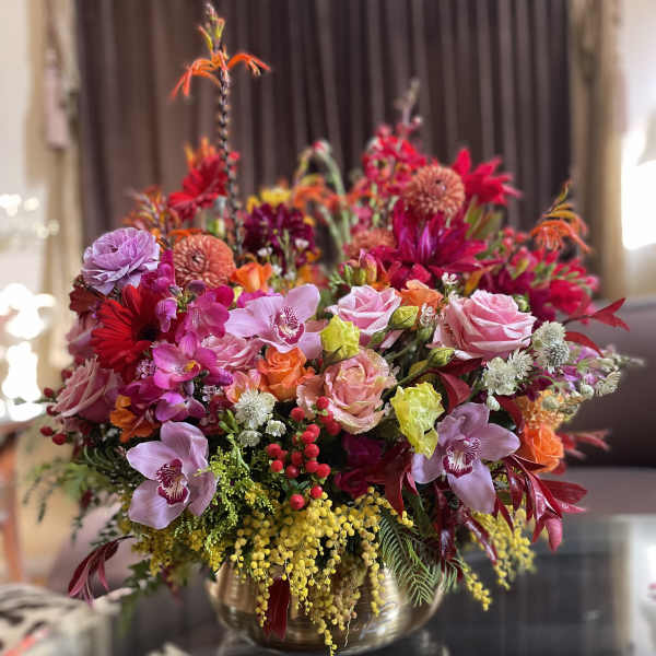 Large mixed bouquet of pink, red, orange, and yellow flowers in a gold vase