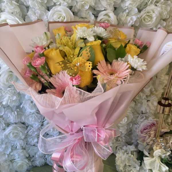 Pink-wrapped bouquet with yellow and pink flowers and a ribbon bow