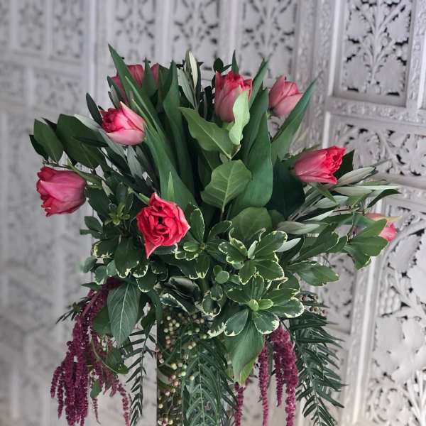 Pink tulips in a clear glass vase with mixed greenery