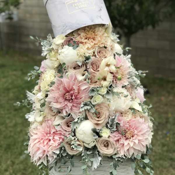 Pastel floral arrangement in a hatbox with pink and cream blooms