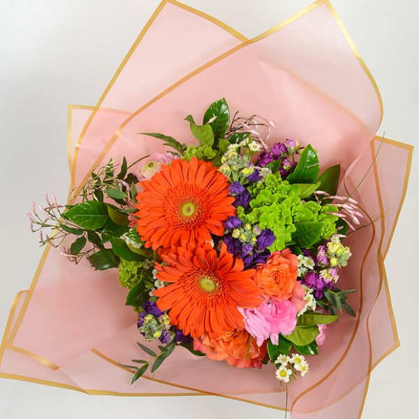 Bouquet of orange gerbera daisies and mixed flowers wrapped in pink paper