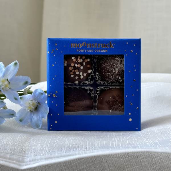 Blue chocolate box with four candies and pale blue flowers beside it