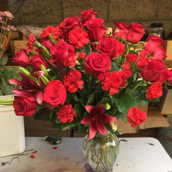 Tall arrangement of red roses, carnations, and lilies in a clear glass vase