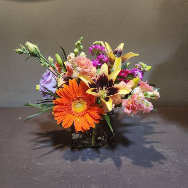 Mixed bouquet in a square glass vase with orange and yellow blooms