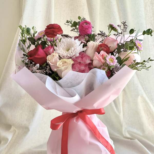 Bouquet of pink and white flowers wrapped in pale pink paper with a red ribbon