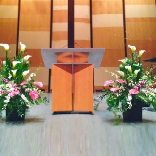 Two large floral arrangements with white calla lilies and pink flowers flanking a wooden podium.