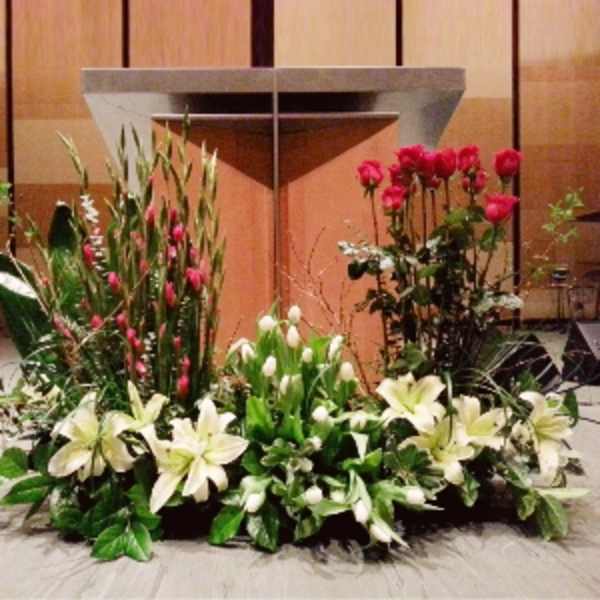Large altar floral arrangement with white lilies, tulips, and red roses in front of a podium