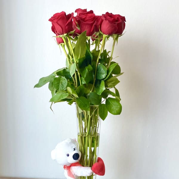 Red roses in a tall glass vase with a small teddy bear attached