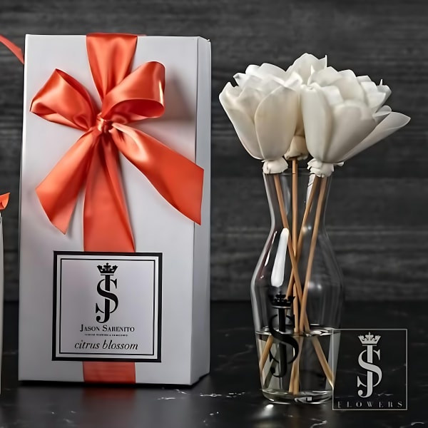 White flowers in a clear vase beside a gift box with a red ribbon.