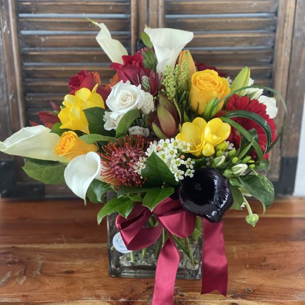 Mixed bouquet in a glass vase with white calla lilies, roses, and bright yellow blooms