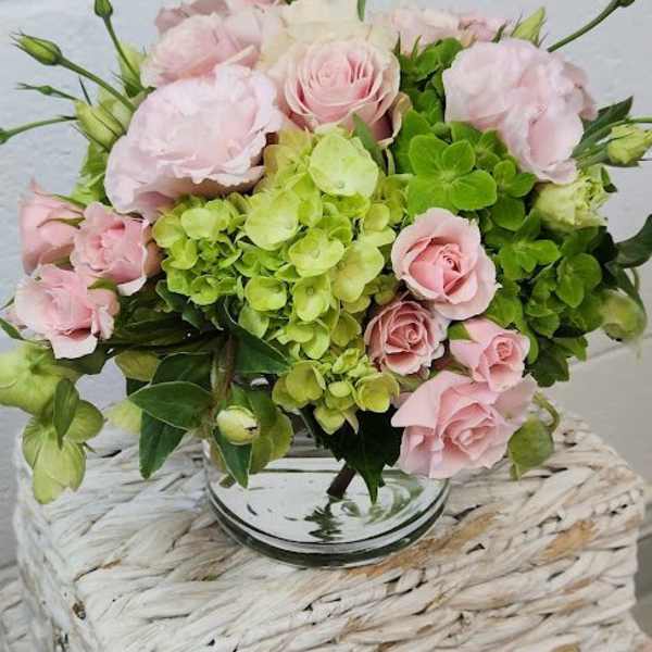 Round arrangement of pale pink roses and green hydrangeas in a clear glass vase