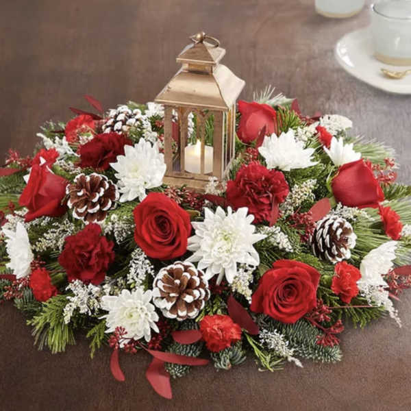 Round floral centerpiece with red roses, white mums, pinecones, and a lantern