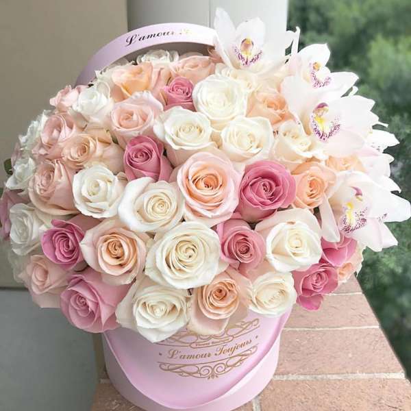 Round box of cream, blush, and pink roses with a few pale orchids in a pink hatbox