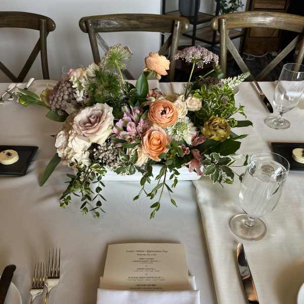 Low floral centerpiece with peach, blush, and white blooms on a dining table