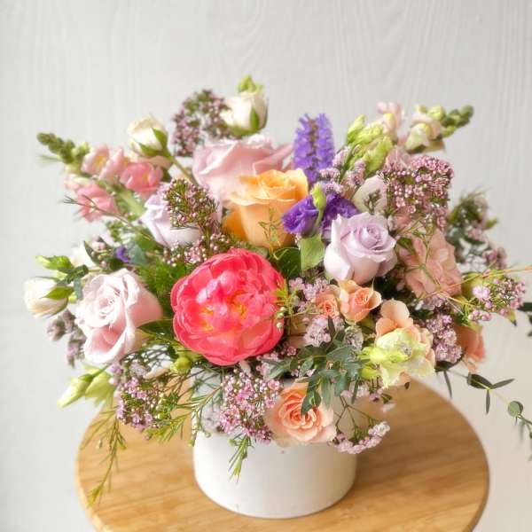 Mixed pastel flower arrangement in a white vase on a wooden stool