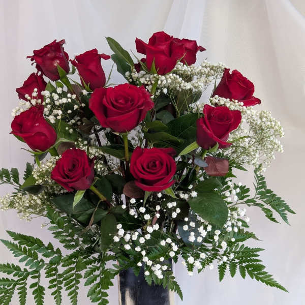 Red roses arranged in a tall silver vase with white baby's breath