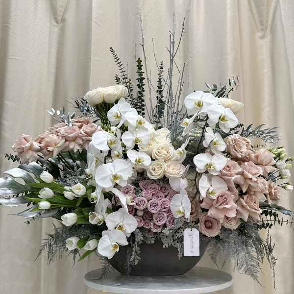 Large pastel floral arrangement with white orchids and blush roses in a black vase