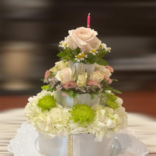 Tiered floral cake with cream roses and white hydrangeas on a doily-lined plate