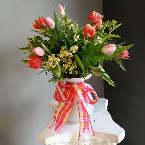 Pink and coral tulips arranged in a white vase with a plaid ribbon