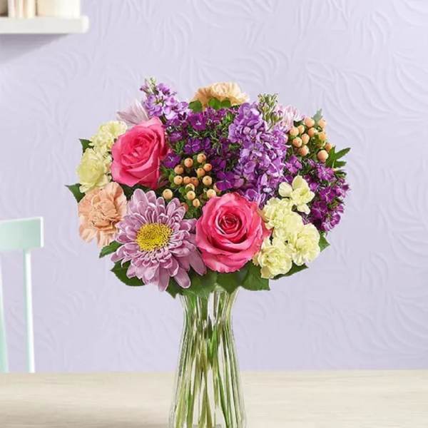 Mixed pink, purple, and cream flowers in a clear glass vase