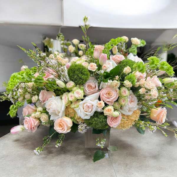 Arrangement of pale pink and white roses with green accents in a clear vase