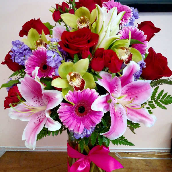 Bouquet of pink lilies, red roses, and purple flowers in a glass vase