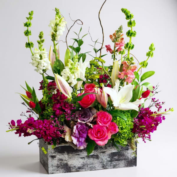 Mixed floral arrangement with pink roses, white lilies, and tall snapdragons in a rustic box