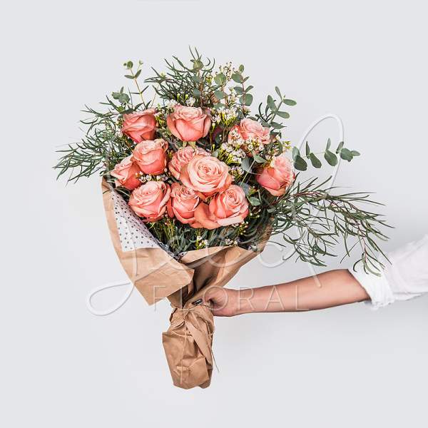 Hand-tied bouquet of peach roses with greenery and small white filler flowers