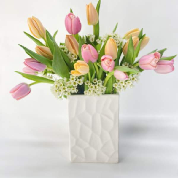 Pink and peach tulips arranged in a white textured vase