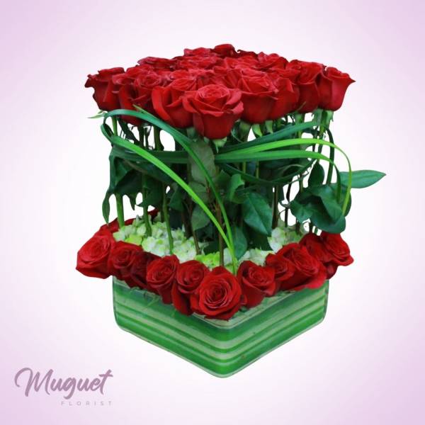 Red roses arranged in a square green vase with ribbon accents
