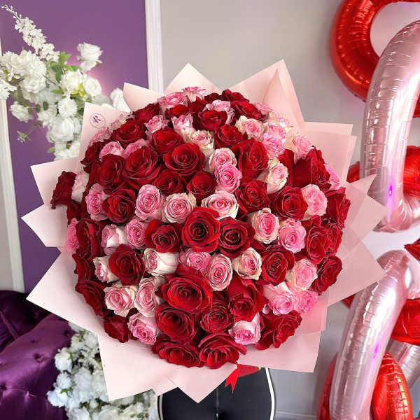 Large round bouquet of red and pink roses wrapped in layered pale pink paper