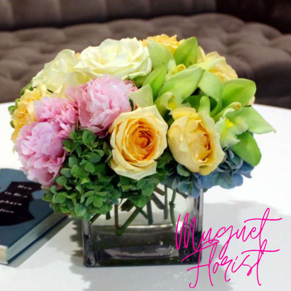 Bouquet of pastel roses, peonies, and orchids in a square glass vase