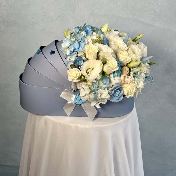 Light blue cradle-shaped box filled with white and blue flowers and a small baby figurine.