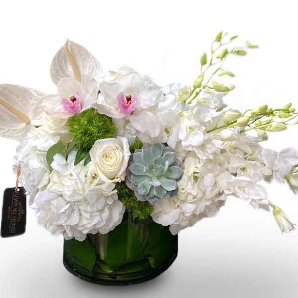 White floral arrangement in a green glass vase with orchids and hydrangeas