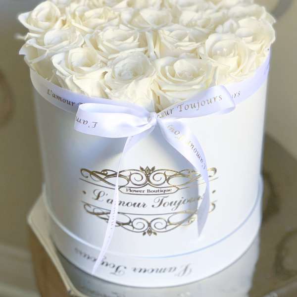 Round white hat box filled with tightly packed white roses and tied with a white ribbon