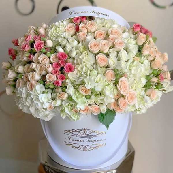 Large hatbox arrangement of pastel roses and white hydrangeas in a white container.