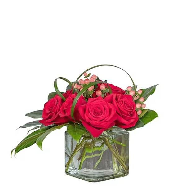 Red roses arranged in a clear glass cube vase with pink berries