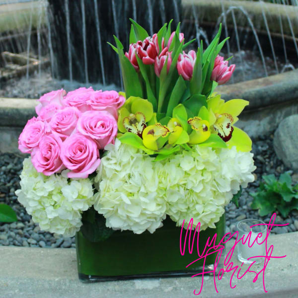 Pink roses, tulips, and green orchids arranged with white hydrangeas in a vase