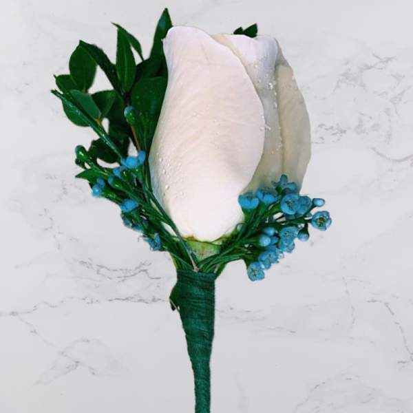 White rose boutonniere with blue accents and green leaves
