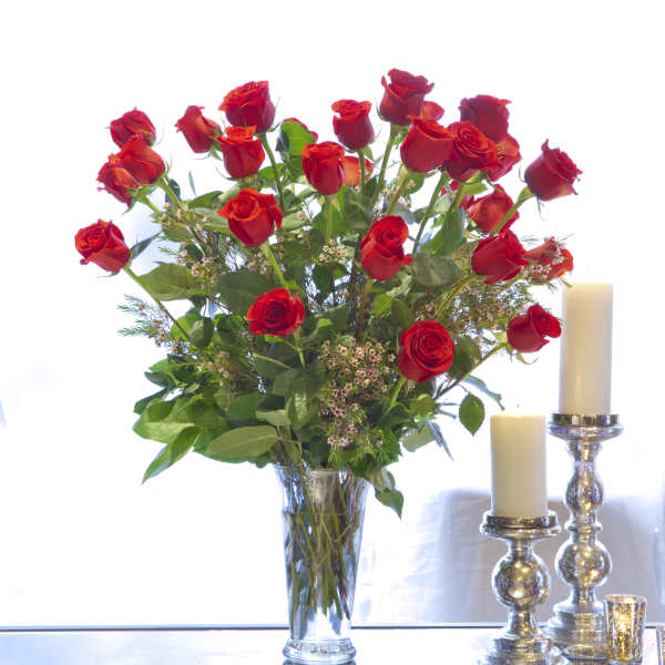 Red roses arranged in a clear glass vase beside white candles