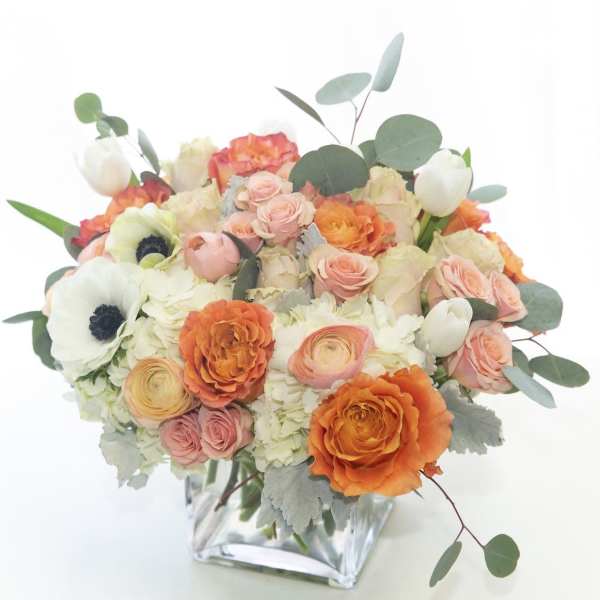 Bouquet of peach, orange, and white flowers in a clear glass vase