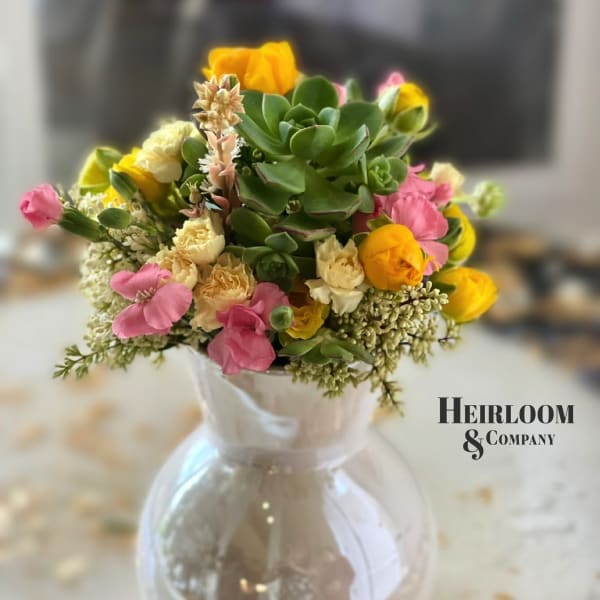 Mixed pink and yellow flowers in a clear glass vase with succulents