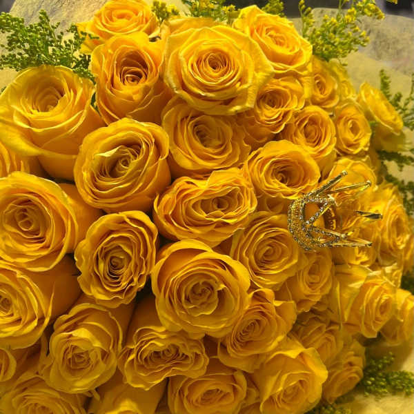 Large bouquet of yellow roses with a small gold crown accent on yellow wrapping