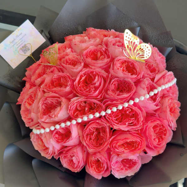 Round bouquet of pink roses wrapped in dark paper with pearl trim